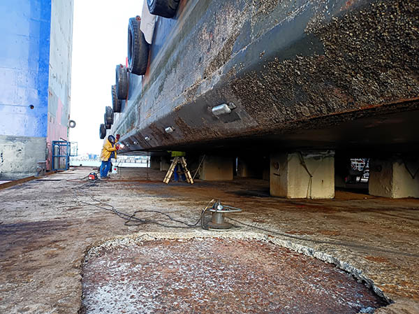 Zwischen Schiff und Dock schleift ein Mann Anbauteile.